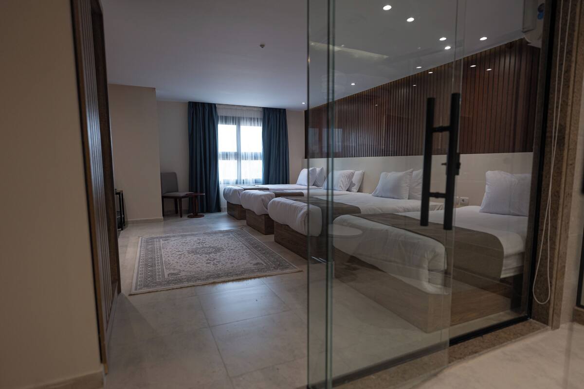 Una habitación de hotel moderna con separador de vidrio, una cama grande, un sofá, un escritorio y vista a la ciudad.