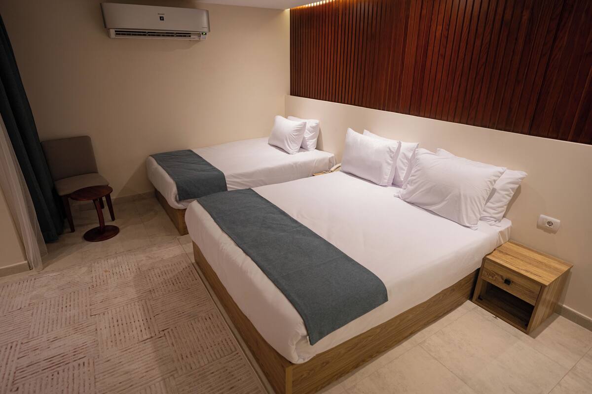 Habitación de hotel con dos camas, cabecera de madera, mesita de noche de madera y una silla.