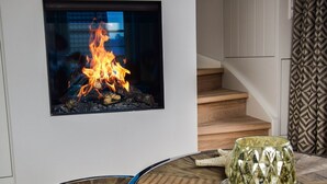 A modern living room with a built-in fireplace, a wooden staircase, and a round glass table with a decorative bowl. - Land in sight with sauna - The best thing about Sylt? The sea. (List)