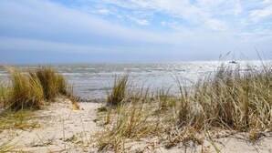 A beach with sand and grass in the foreground and a boat in the water in the background. - Land in sight with sauna - The best thing about Sylt? The sea. (List)