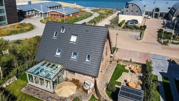 A modern building with a glass conservatory, a patio with outdoor furniture, and a view of the sea. - Land in sight with sauna - The best thing about Sylt? The sea. (List)