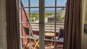 A room with a large window overlooking a coastal area, featuring a wooden chair and a small round table. - Land in sight with sauna - The best thing about Sylt? The sea. (List)