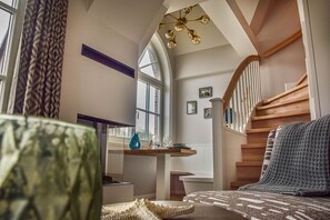 A spacious living room with a large window, a wooden staircase, and a modern chandelier.