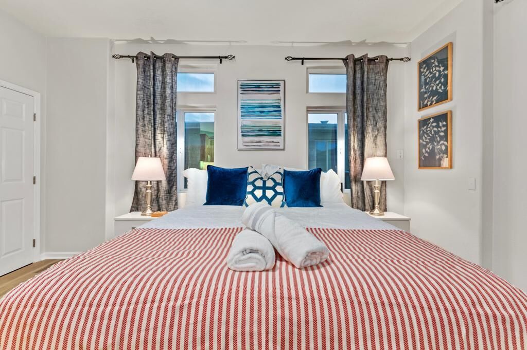 Ein Hotelzimmer mit einem großen Bett, zwei Nachttischlampen, einem fenster mit Vorhängen und einem gerahmten Kunstwerk an der Wand.