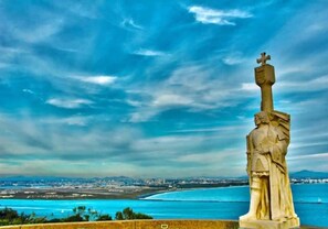 Uma estátua com vista para uma paisagem urbana costeira sob um céu claro.