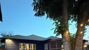 A house with a gravel yard, a wooden picnic table, and string lights.
