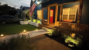 A modern house with a red door, a flag, and a well-lit front yard.