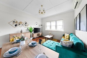 A modern living room with a dining table set, a sofa, a TV, and a window.