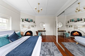A bedroom with a fireplace, a bed with blue bedding, a desk, and a mirror. - Art Deco Hideaway - St Kilda (St Kilda)