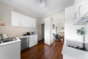 A modern kitchen with white cabinets, a dishwasher, and a microwave. There is a dining area with a table and chairs.