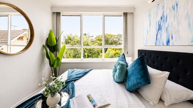 A bedroom with a bed, a window, a mirror, and a painting. - The Meadow Gardens Oasis (St Kilda East)