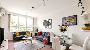 A modern living room with a sofa, coffee table, and dining area. - The Meadow Gardens Oasis (St Kilda East)