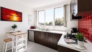 A modern kitchen with a window, a dining area with a table and chairs, and a red-tiled backsplash. - The Meadow Gardens Oasis (St Kilda East)