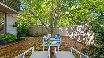 A patio with two wicker chairs, a table, and a couch with cushions.