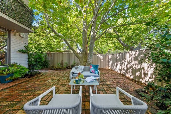 A patio with two wicker chairs, a table, and a couch with cushions.