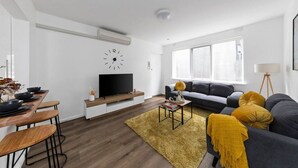 Una sala de estar moderna con un televisor de pantalla plana, un sofá, una mesa de comedor y un ventanal grande.