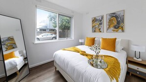 Un dormitorio con cama, ventana, espejo y obras de arte en la pared.