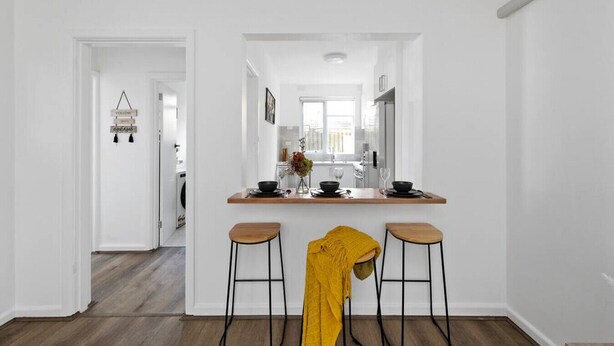 Una cocina moderna con una isla central, dos taburetes y un plaid amarillo en uno de ellos.