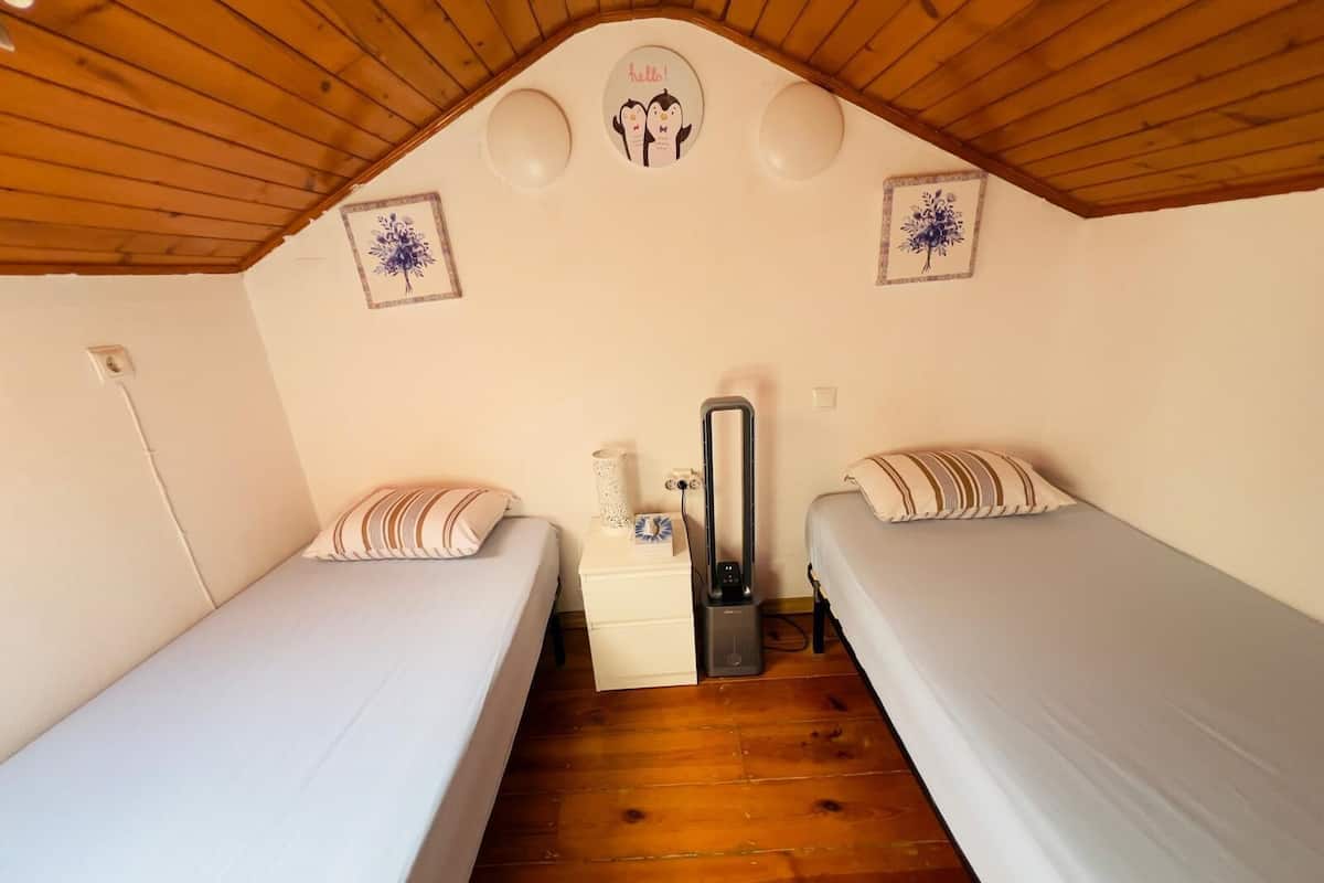 Ein Zimmer mit zwei Einzelbetten, einer Holzbalkendecke und einem kleinen Nachttisch mit Lampe.