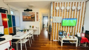 Ein Hotelzimmer mit Holzboden, einem Fernseher, einem Schreibtisch mit Büchern, einem roten Tisch und Schließfächern.
