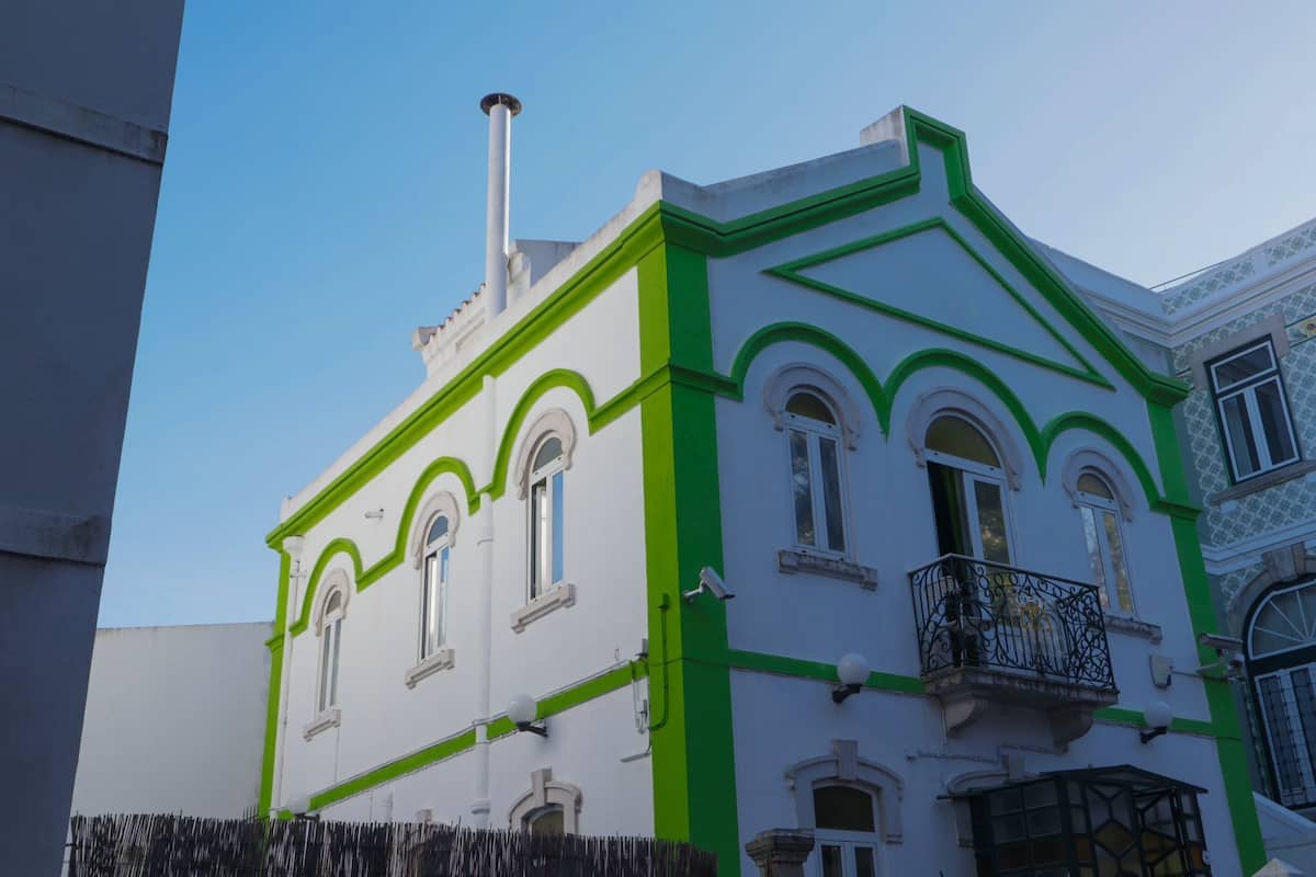 Ein Gebäude mit weißer Fassade und grünen Verzierungen, mit Bogenfenstern und einem Balkon mit aufwendigen Geländern.