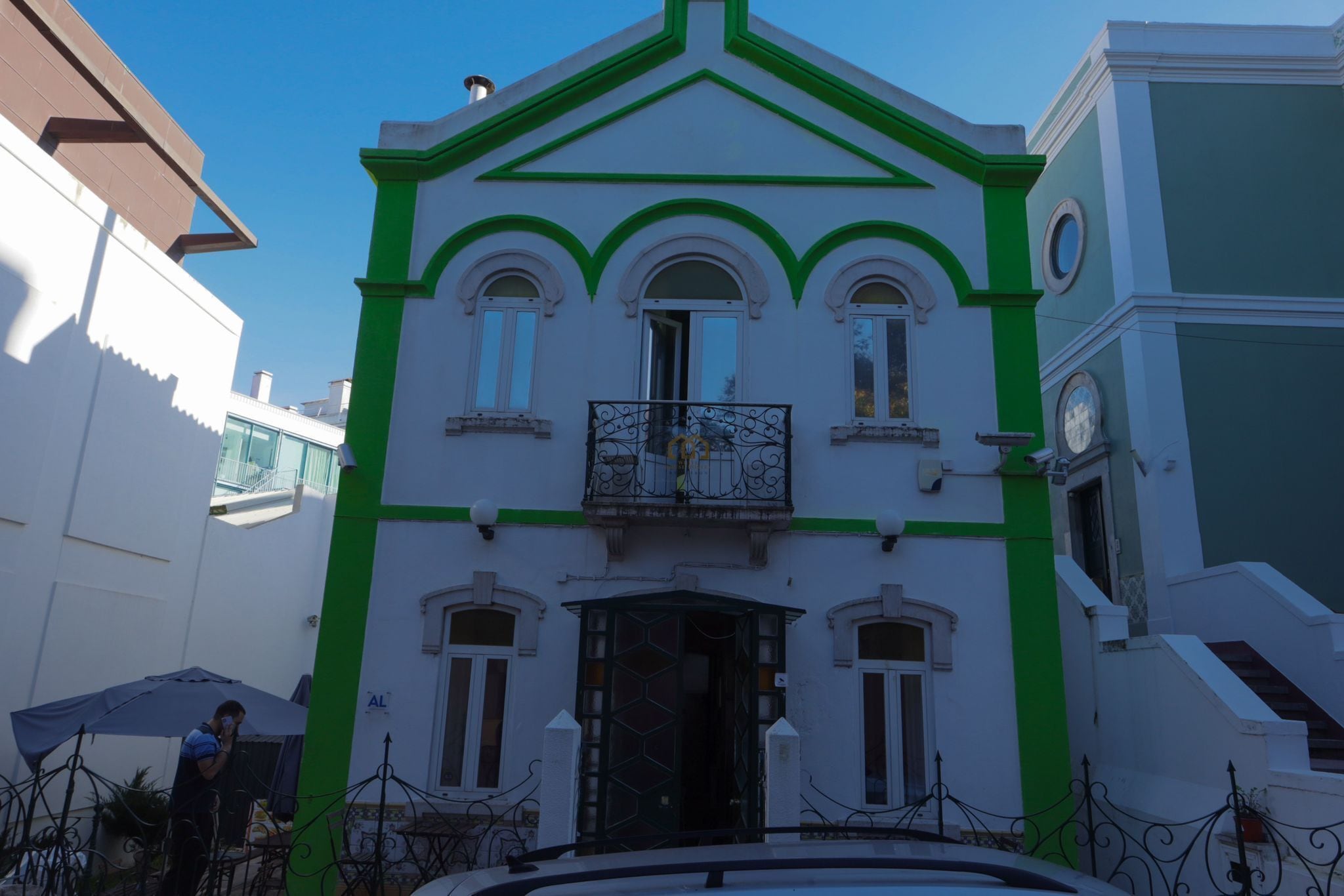 A building with a green and white facade, a balcony with a wrought iron railing, and a door with a geometric pattern.