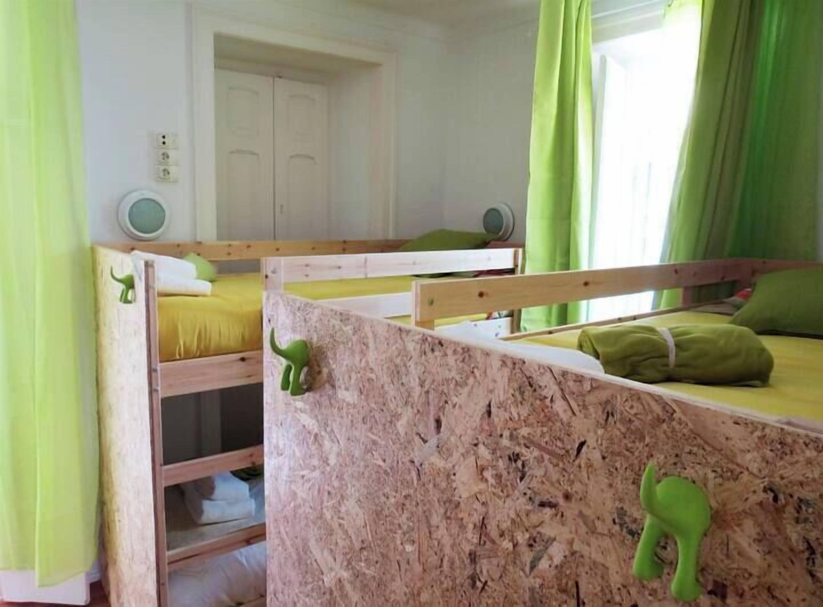 Ein Schlafzimmer mit Etagenbetten, grünen Vorhängen, einer weißen Tür und einem kleinen runden Tisch mit Lampe.