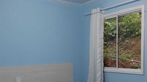 Un dormitorio con cama, una ventana con cortina y una lámpara en el techo.