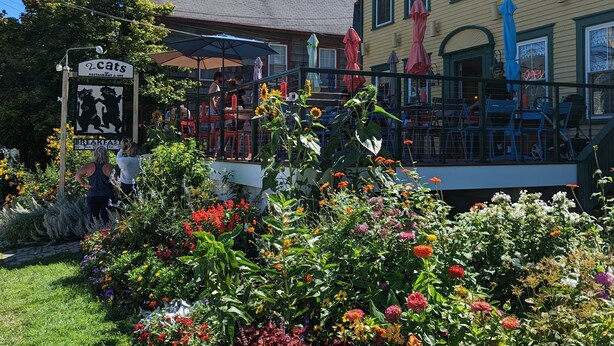 A restaurant with outdoor seating, surrounded by a garden with various flowers. - Historic 2 Cats Inn (Bar Harbor)