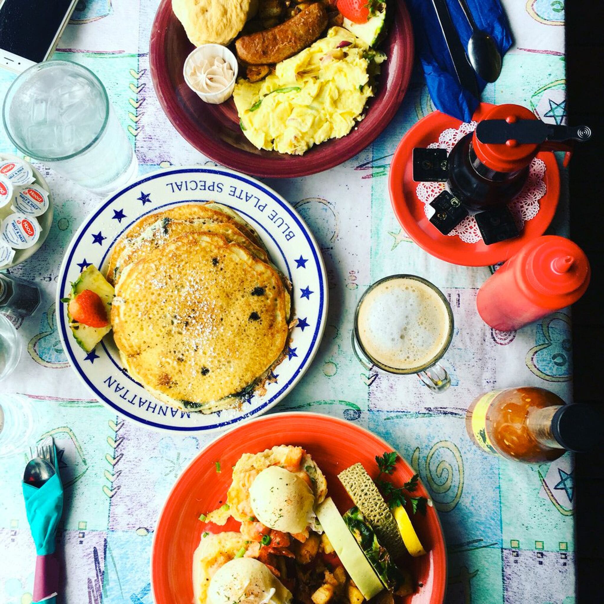 A table with various breakfast items including pancakes, sausages, and a plate of scrambled eggs.
