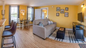A living room with a sofa, chairs, a coffee table, a TV, and a dining area with a table and chairs. - Historic 2 Cats Inn (Bar Harbor)