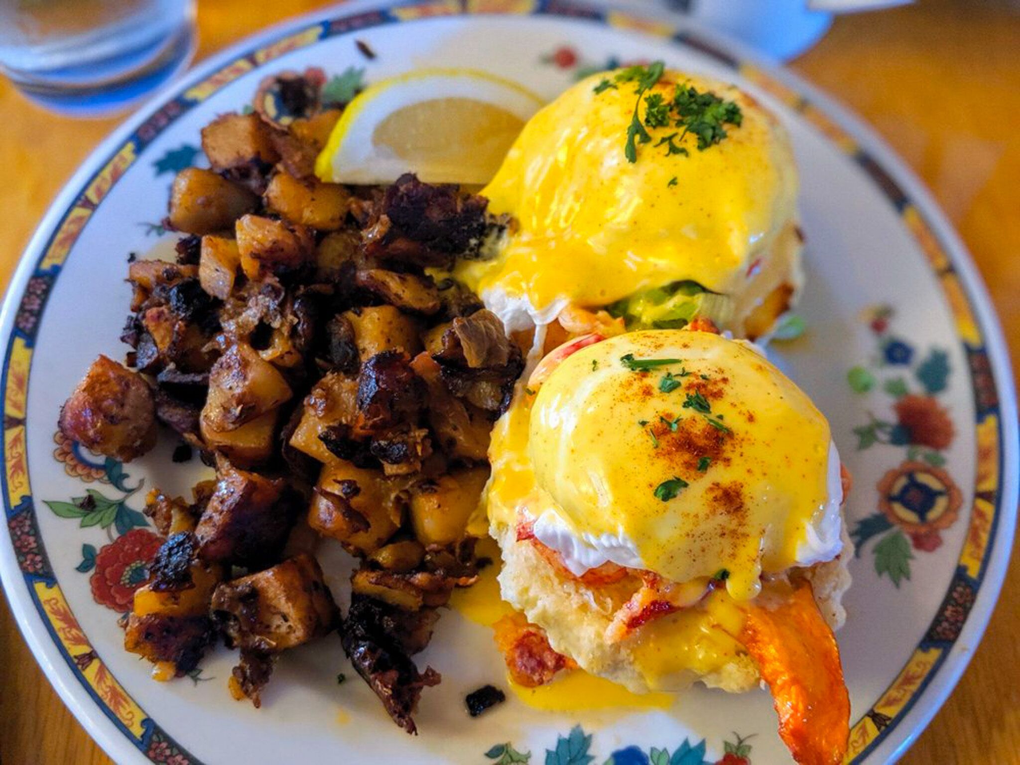 A plate with eggs benedict, hash browns, and a slice of lemon.