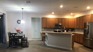 A modern kitchen with wooden cabinets, a central island, stainless steel appliances, and a dining area with a table and chairs. - Family house in Kissimmee. (Kissimmee)