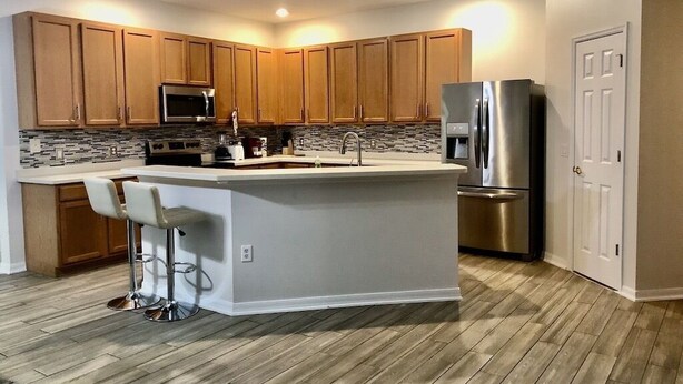 A modern kitchen with wooden cabinets, a stainless steel refrigerator, and a central island with bar stools. - Family house in Kissimmee. (Kissimmee)