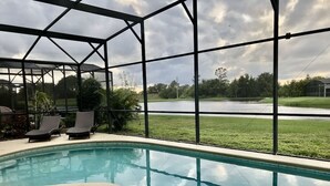 A swimming pool with a view of a lake, surrounded by a covered area with chairs. - Family house in Kissimmee. (Kissimmee)