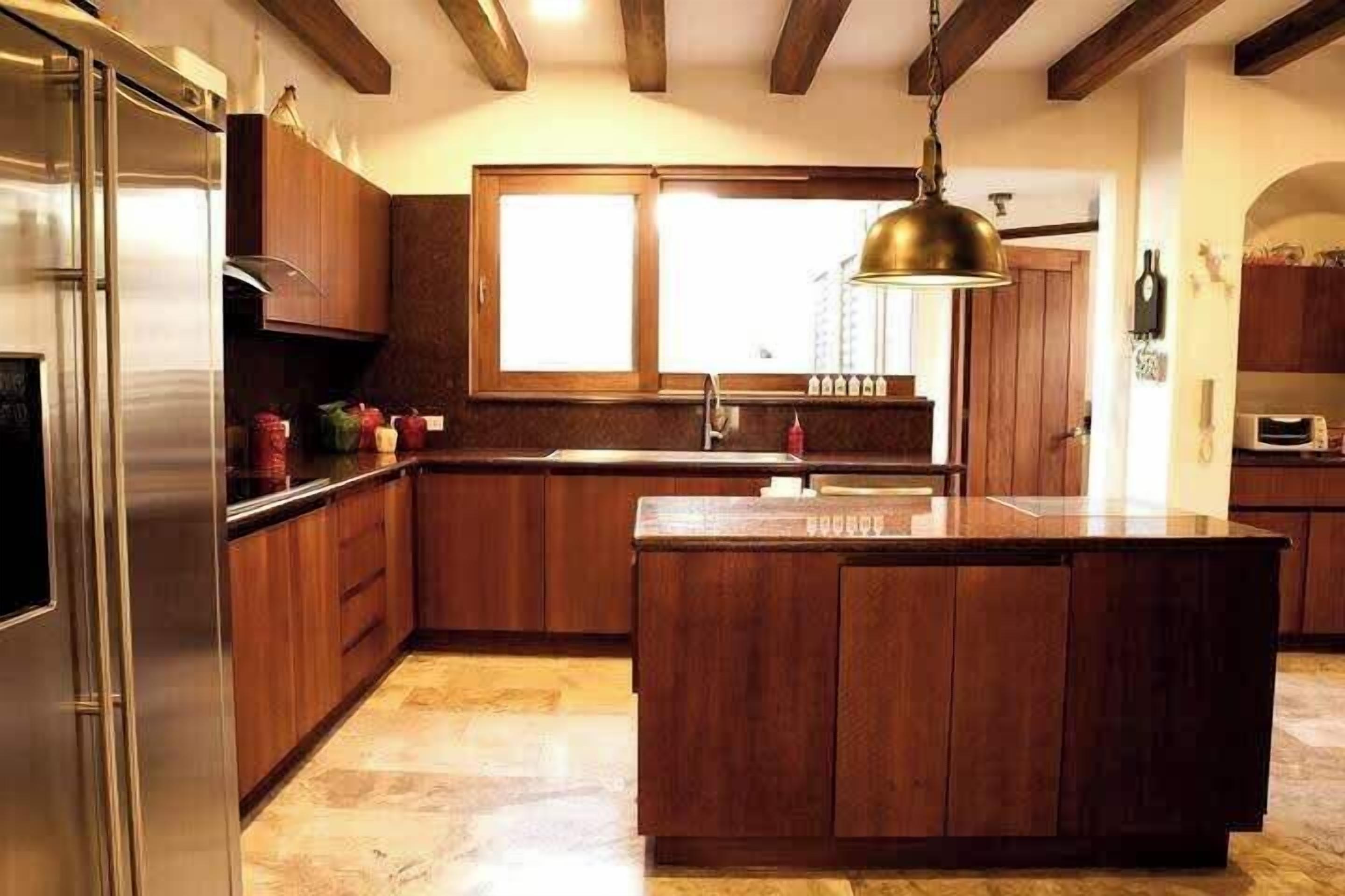 Une cuisine dotée de meubles en bois, d’un réfrigérateur en acier inoxydable, d’un grand îlot central et d’un luminaire suspendu.