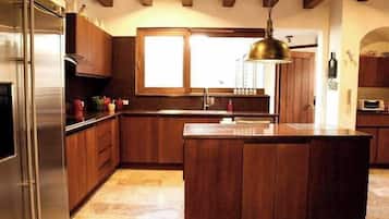 Une cuisine dotée de meubles en bois, d’un réfrigérateur en acier inoxydable, d’un grand îlot central et d’un luminaire suspendu.