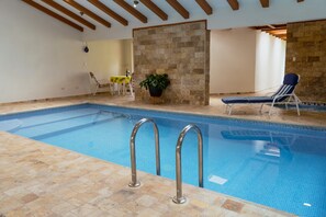 An indoor swimming pool with clear blue water, a stone-tiled floor, and a wooden ceiling.