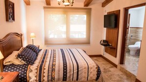 Une chambre à coucher avec un lit, une télévision, une fenêtre et une salle de bain visible à travers une porte ouverte.