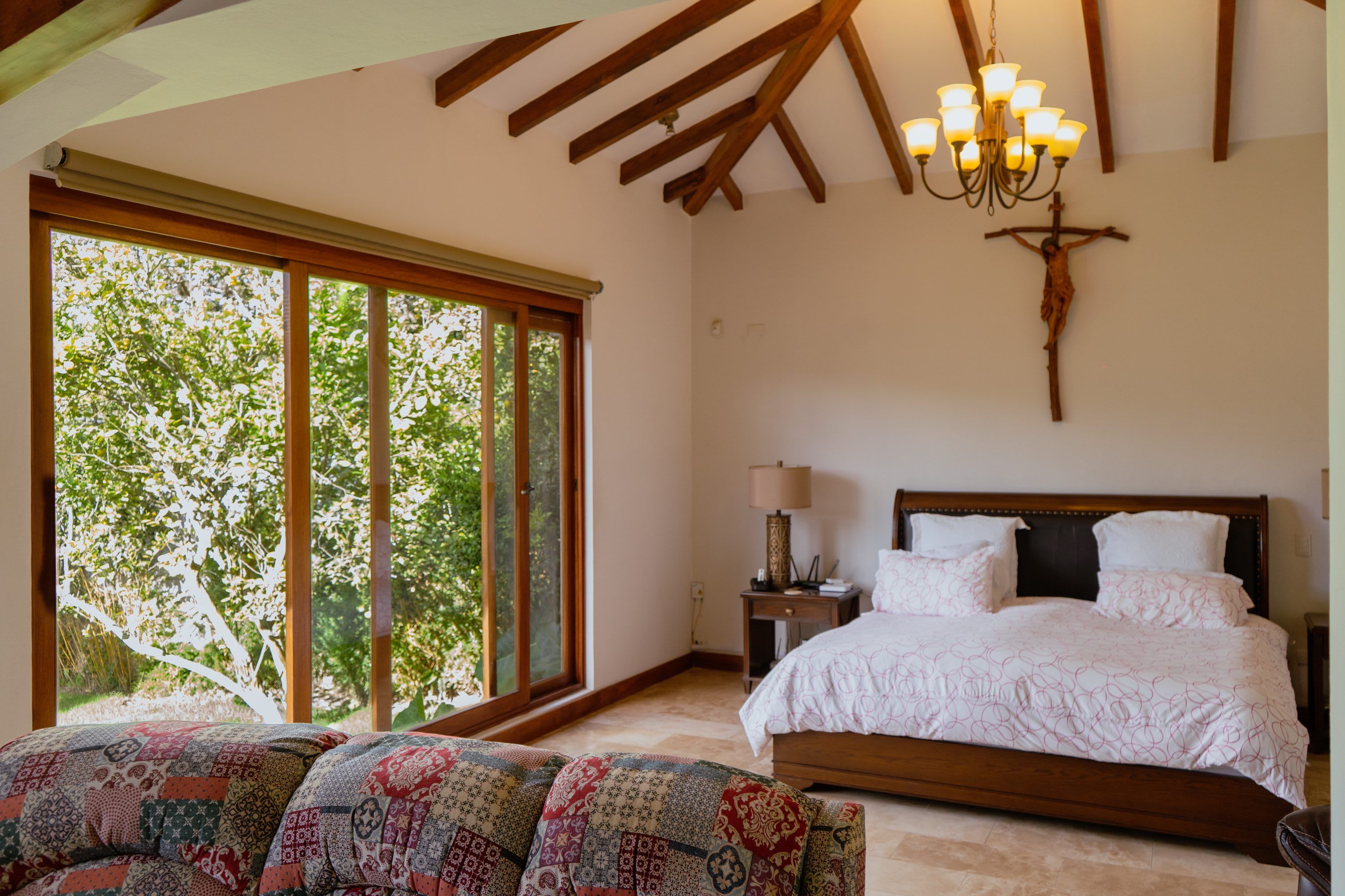 A bedroom with a large window, a bed, a nightstand, and a chandelier.