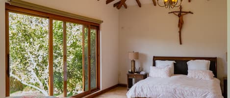 A bedroom with a large window, a bed, a nightstand, and a chandelier.