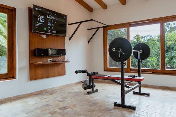 A gym with a TV mounted on the wall, a bench press, and a squat rack.