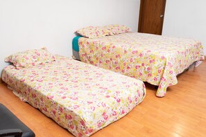 A room with two single beds, each with a floral bedspread, a wooden floor, and a door in the background. - Guayllabamba Estate - Indoor Pool, Jacuzzi & Gym (Quito)