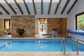 An indoor swimming pool with a clear view of the ceiling, stone walls, and a lounge chair. - Guayllabamba Estate - Indoor Pool, Jacuzzi & Gym (Quito)