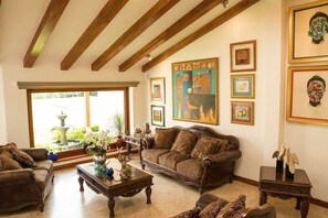A living room with a brown leather sofa, a coffee table, and a large painting on the wall. - Guayllabamba Estate - Indoor Pool, Jacuzzi & Gym (Quito)