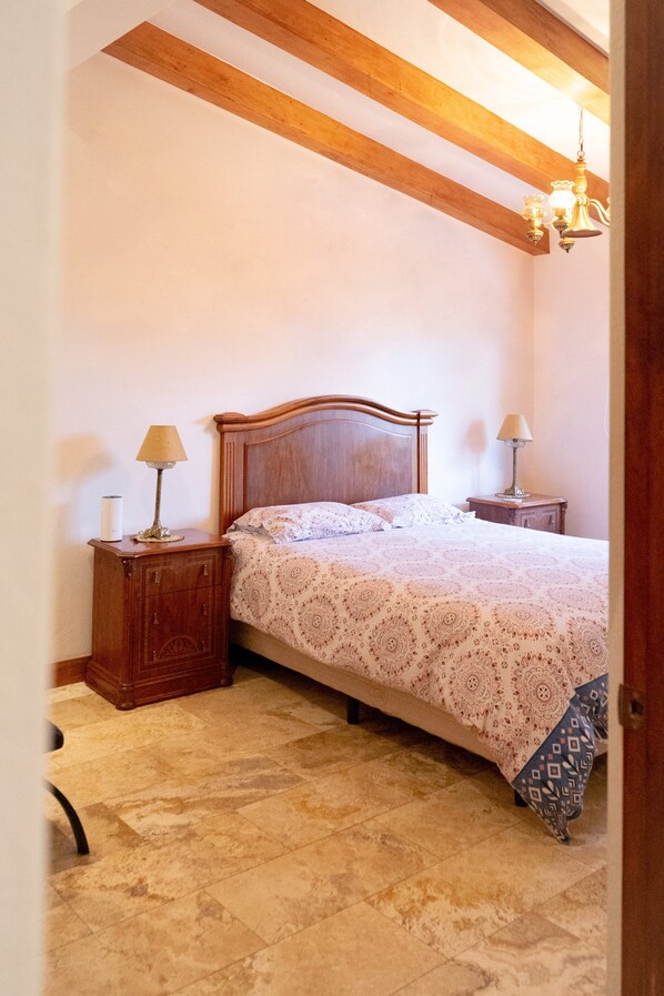 A bedroom with a wooden headboard, a patterned bedspread, two bedside tables with lamps, and a chandelier.