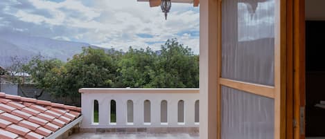 Un balcon doté d’un sol carrelé, d’une balustrade blanche ornée d’arcatures, et offrant une vue sur des arbres et des montagnes en arrière-plan.