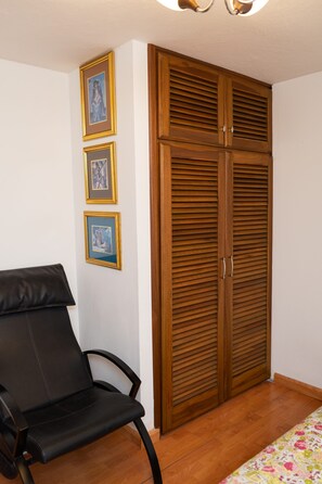 A room with a wooden wardrobe, a black chair, and three framed pictures on the wall. - Guayllabamba Estate - Indoor Pool, Jacuzzi & Gym (Quito)