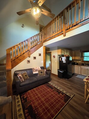 A living room with a wooden staircase, a black sofa, a patterned rug, and a ceiling fan. - Cozy cabin Peaceful Side, Townsend, TN, Laurel Valley,  no steep roads (Townsend)