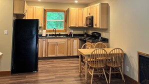 A spacious kitchen with wooden cabinets, a black refrigerator, and a dining area with wooden chairs. - Cozy cabin Peaceful Side, Townsend, TN, Laurel Valley,  no steep roads (Townsend)